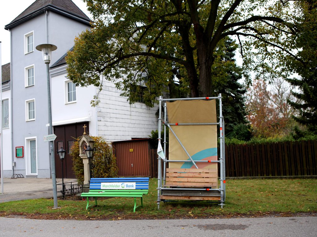 Neben einer Kirche steht eine Bank mit einem QR Code, um das Interview zu hören.